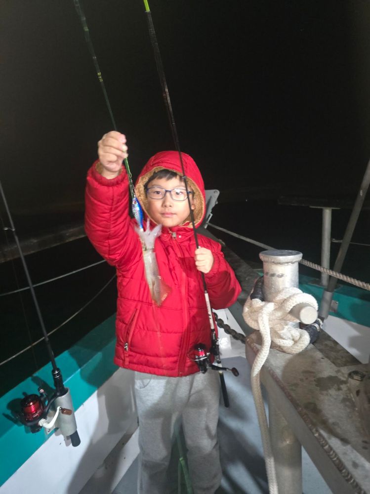Child on boat holding fishing rod with small catch, wearing red jacket and glasses.