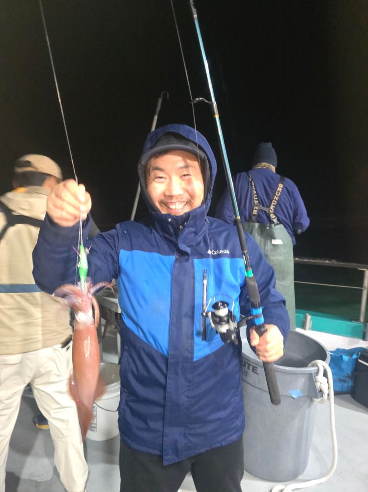 Person in a blue jacket holding a fishing rod and a squid on a boat at night.