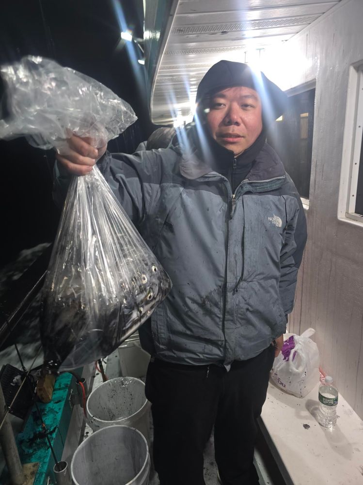 Person in jacket holding a bag of fish on a boat at night.