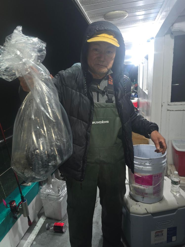 Person in hooded jacket holding a clear plastic bag on a boat at night.