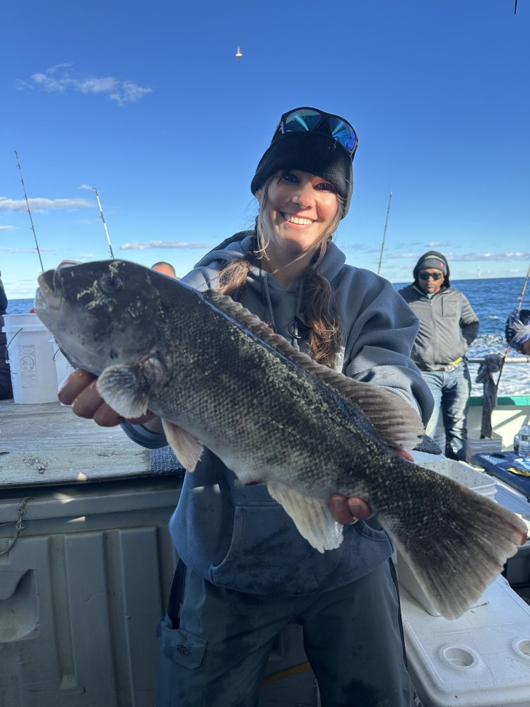 Person holding a large fish on a boat with blue sky and sea in the background.