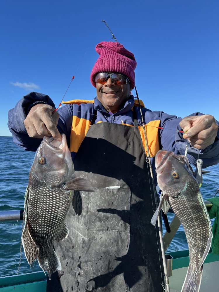 Person in pink hat holding two fish on a boat under a clear blue sky.