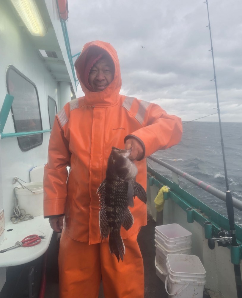 Person in orange raincoat holding a fish on a boat under cloudy sky.