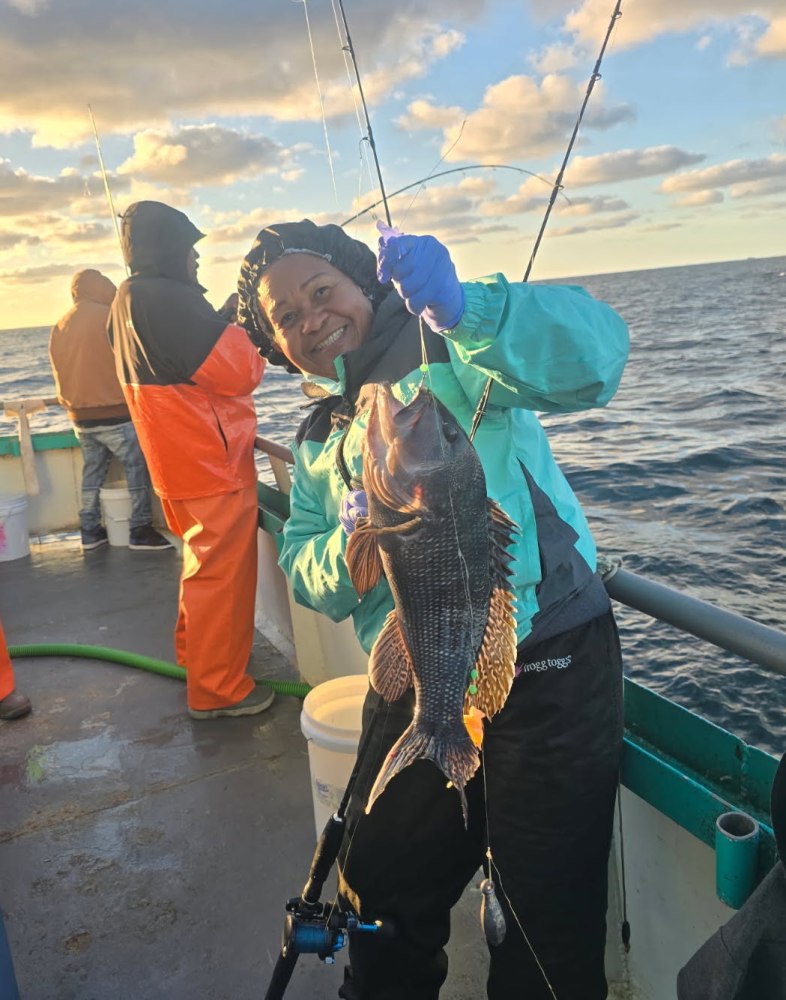 Person in a teal jacket holding a fish on a boat with a cloudy sky.