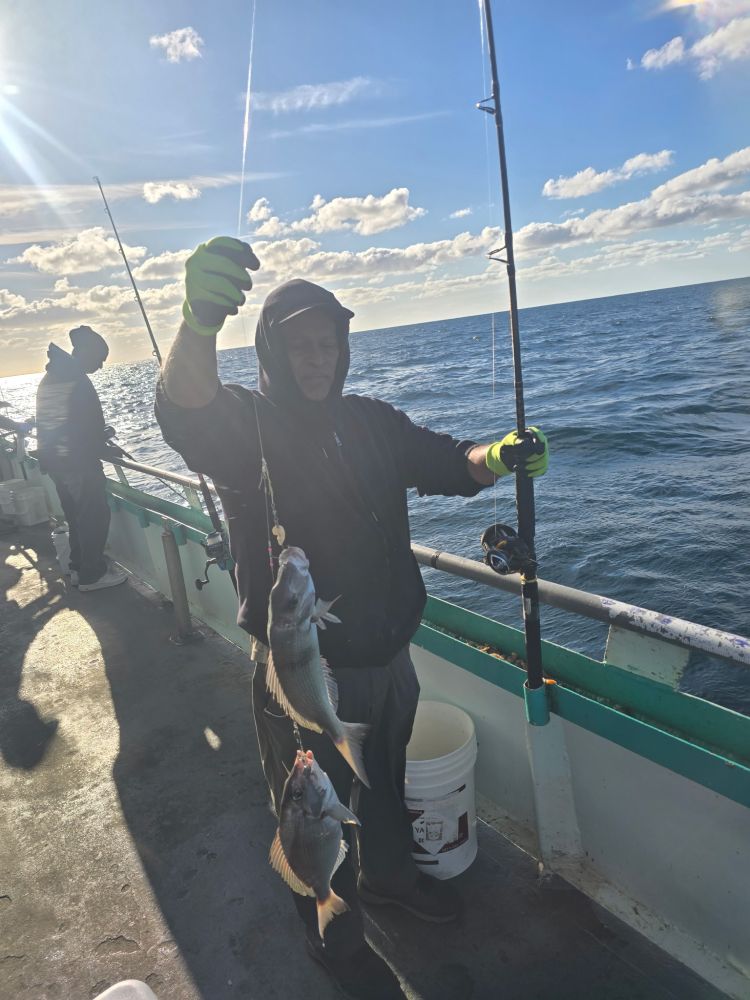 Person on boat holding two fish on a line, with ocean and cloudy sky in the background.