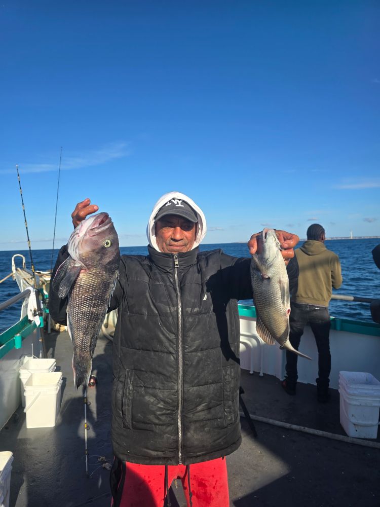 Person on a boat holding two fish against a clear blue sky.