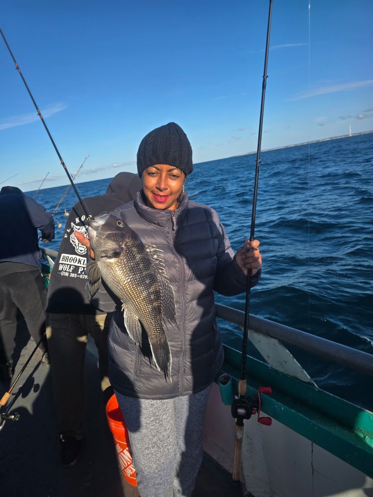 Person on a boat holding a fish with a fishing rod on a sunny day.