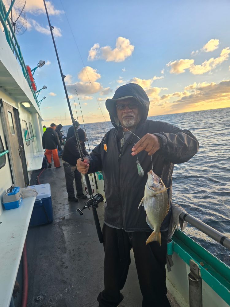 Man holding a fish on a boat, sunset in the background over the ocean.