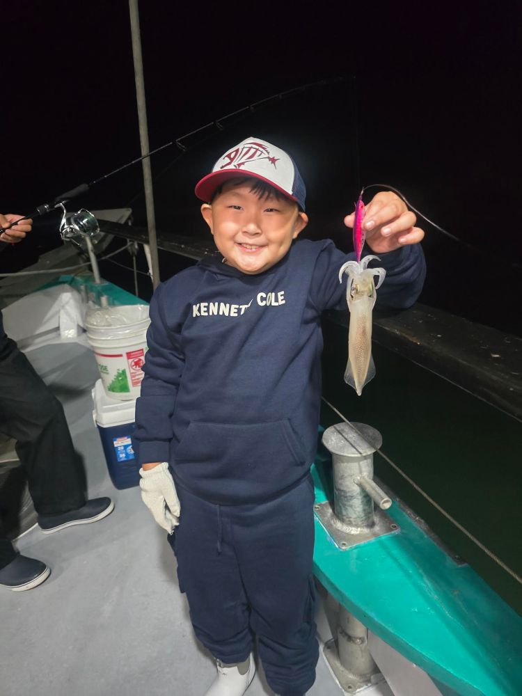 Child on boat holds a small squid, smiling at night.