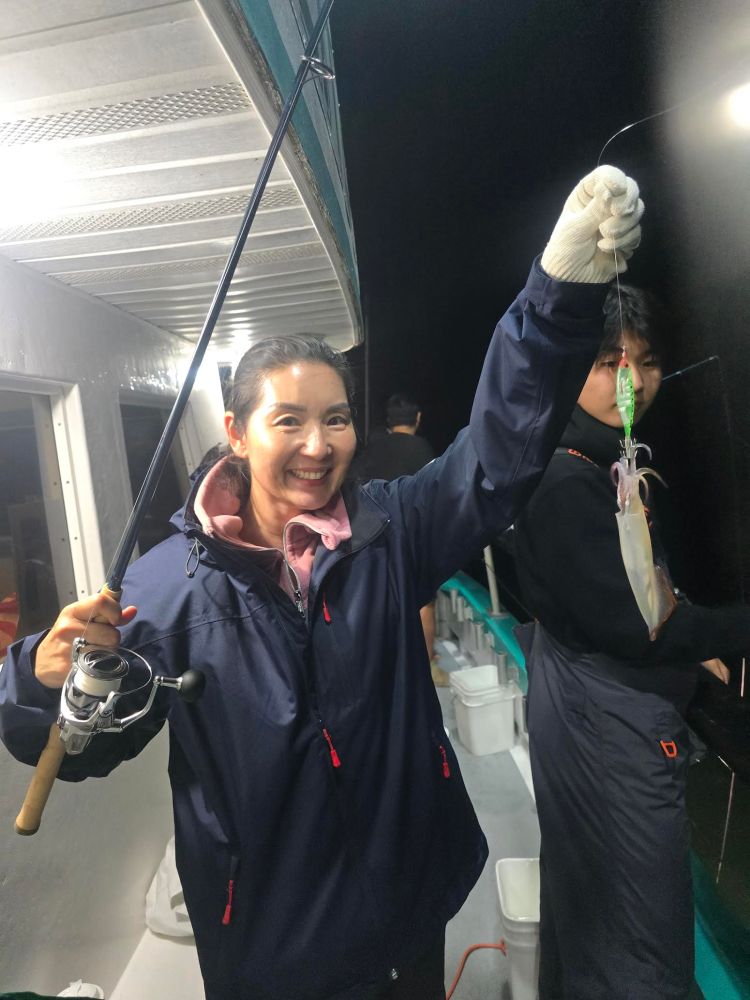Person holding a fishing rod with a squid on the line, smiling on a boat at night.