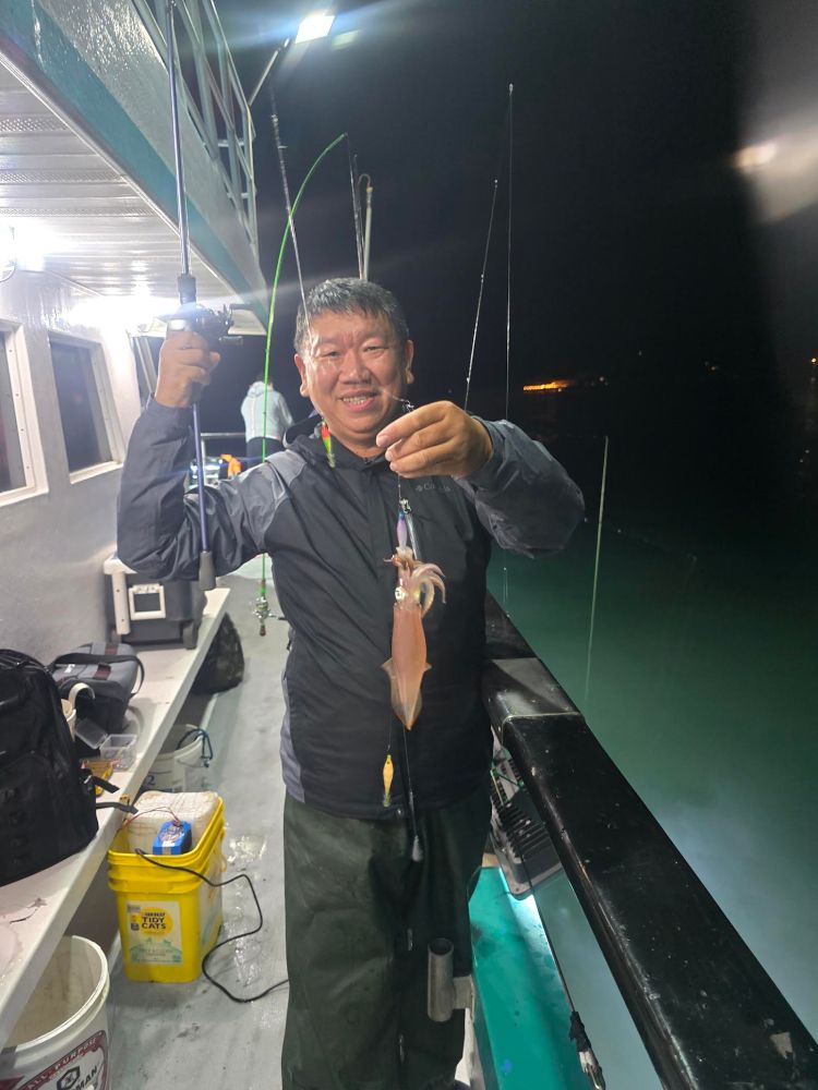Person on a boat holding a fishing rod with a caught squid during nighttime.