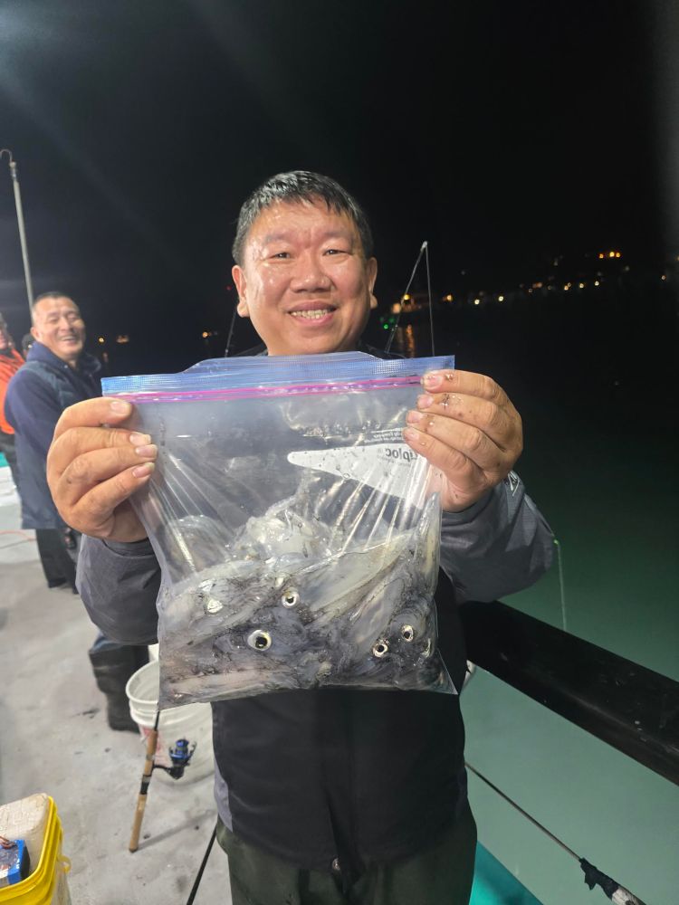 Man smiling and holding a bag filled with squid on a fishing pier at night.