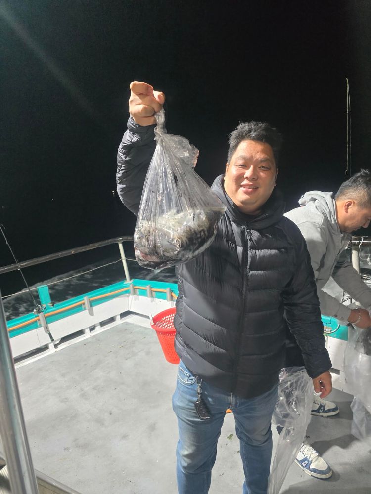 Smiling person on a boat at night holding a bag of fish.