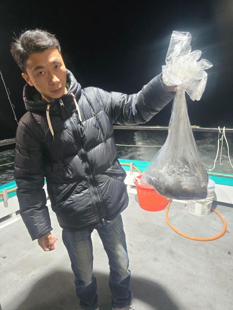 Person holding a clear plastic bag with contents on a boat deck at night.
