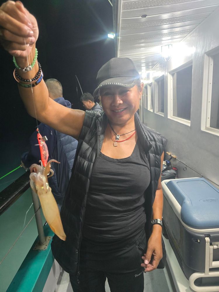 Person on a boat at night, holding a squid on a fishing line, smiling at the camera.