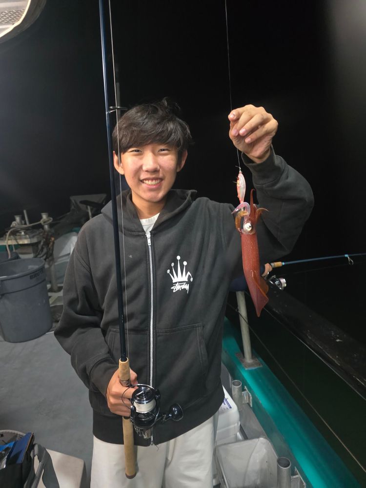 Person smiling while holding a fishing rod with a squid on a boat at night.