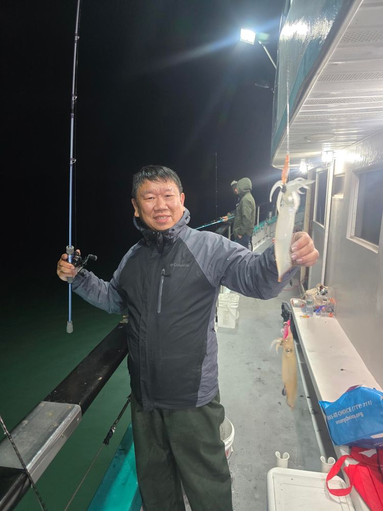 Person holding a fishing rod and a caught squid on a boat at night.