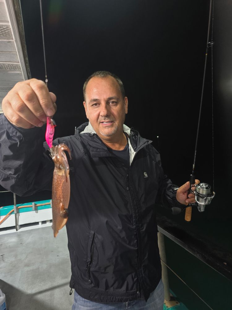 Person holding a fishing rod and a caught squid on a boat at night.