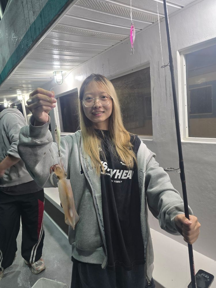 Person holding a squid on a fishing line inside a boat.