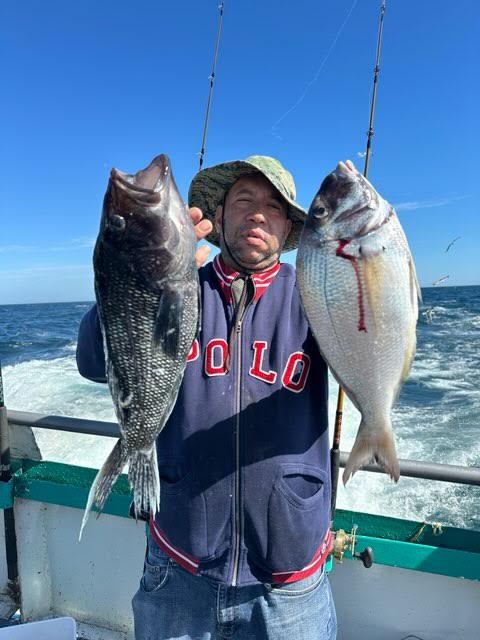 Person on a boat holding a black fish and a silver fish, with blue sky and ocean in the background.
