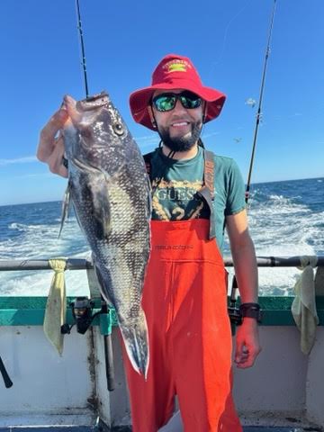 Person in red hat holding a large fish on a boat with ocean in the background.