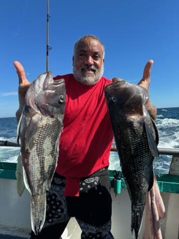 Man in red shirt holding two large fish on a boat.