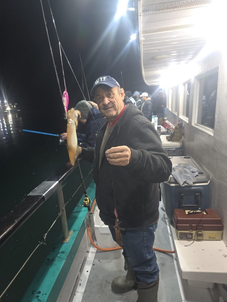 Person holding a squid on a fishing boat at night.