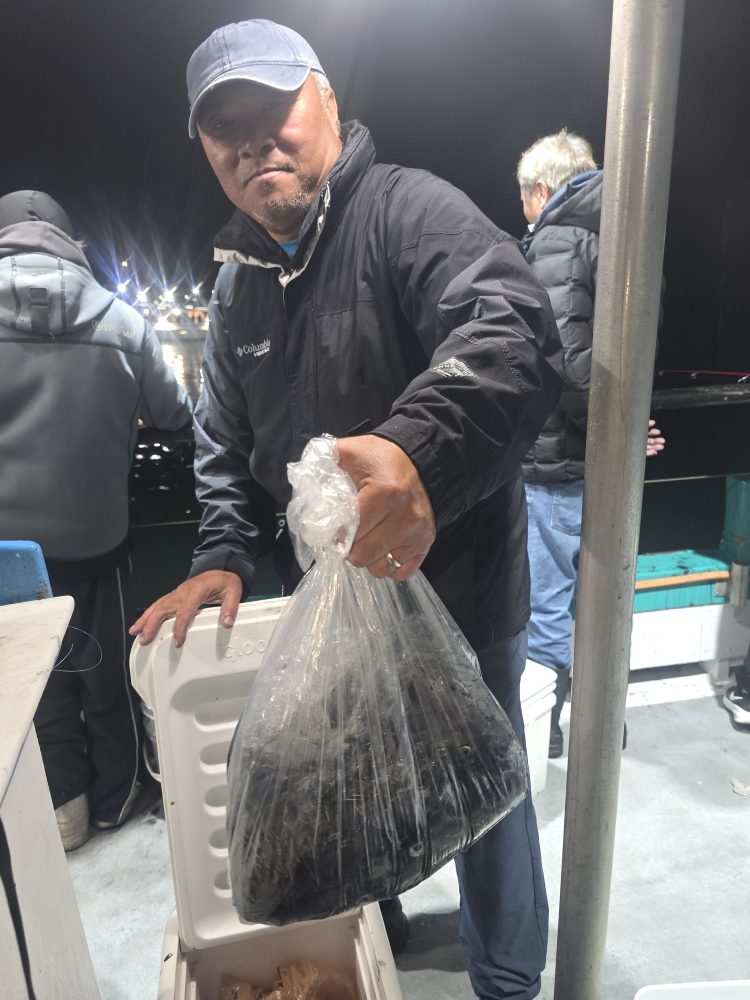 Person holding a bag of fish in a boat at night, opening a cooler.