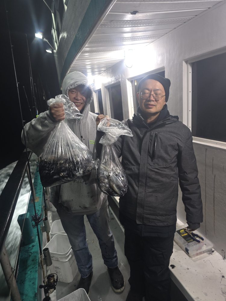 Two people on a boat holding bags of fish at night.