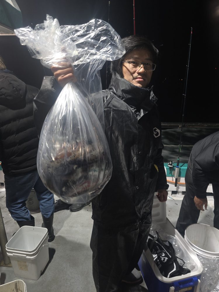 Person holding a bag of fish on a boat at night, wearing a dark raincoat.