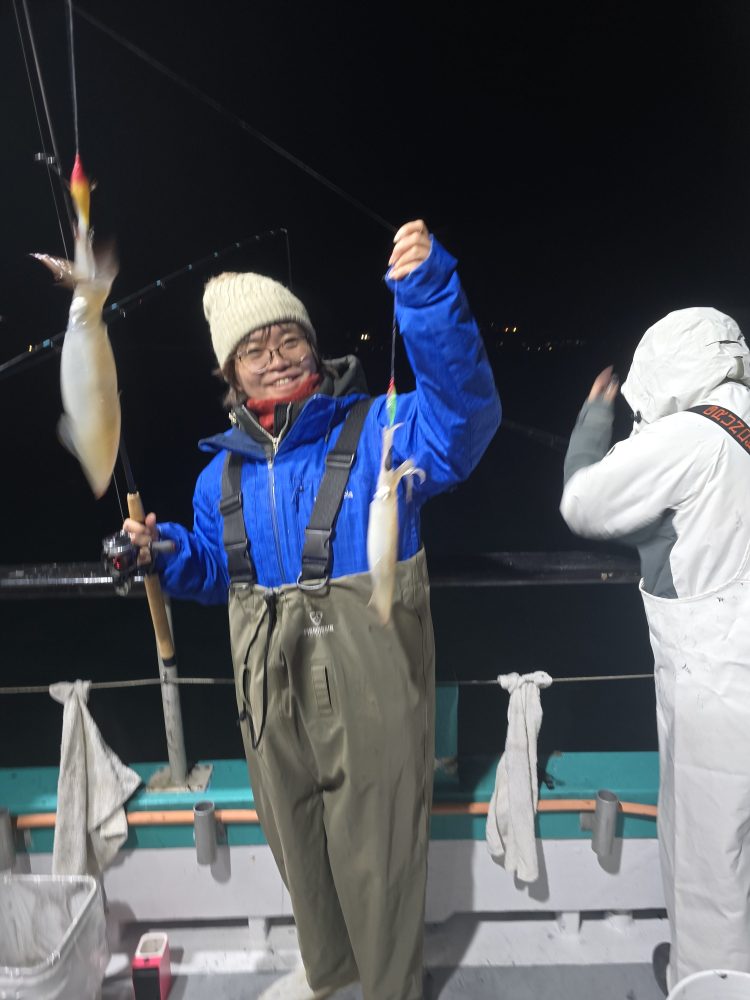 Person in blue jacket and waders holds a squid on a fishing boat at night.