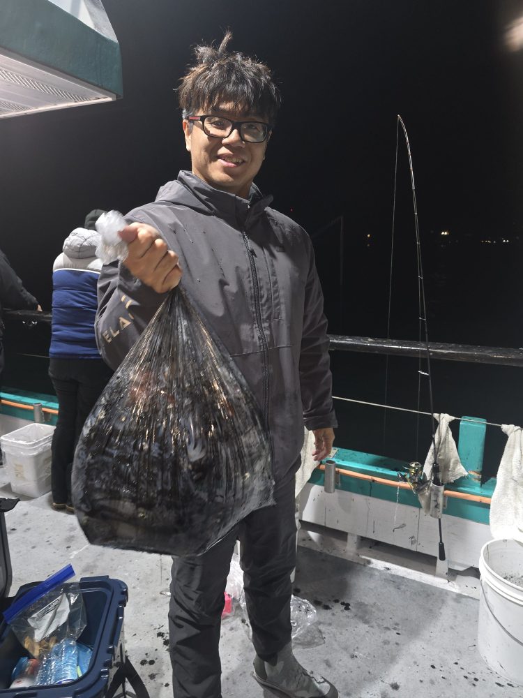 Person holding a bag of fish on a boat at night with fishing rod nearby.