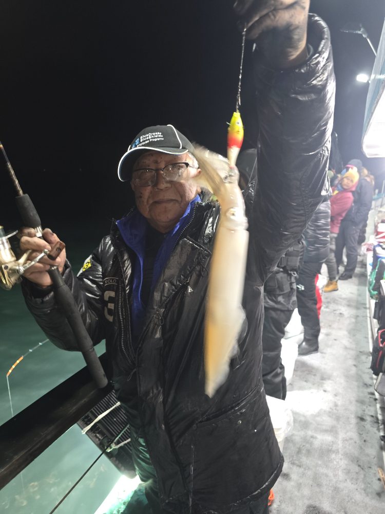 Person holding a fishing rod and a caught squid on a boat at night.