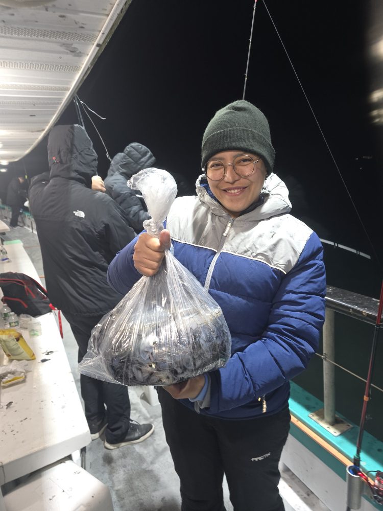 Person in a blue jacket and beanie holds a bag of fish on a boat at night.