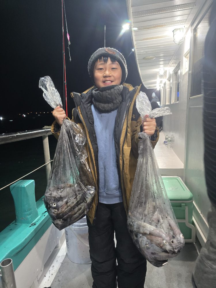 Child on boat holding two bags of caught fish, smiling at night.
