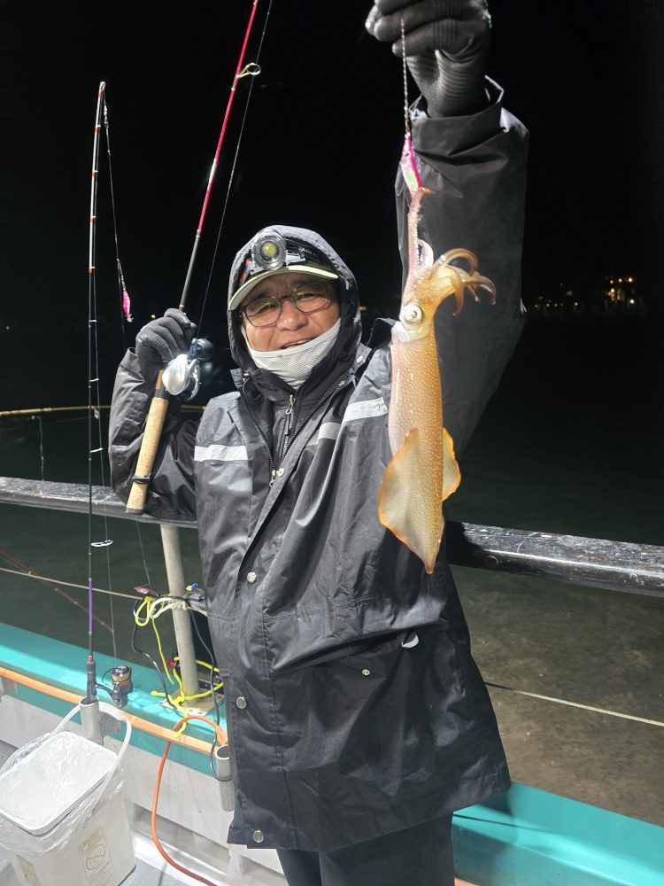 Person in a raincoat holding a squid on a fishing boat at night.