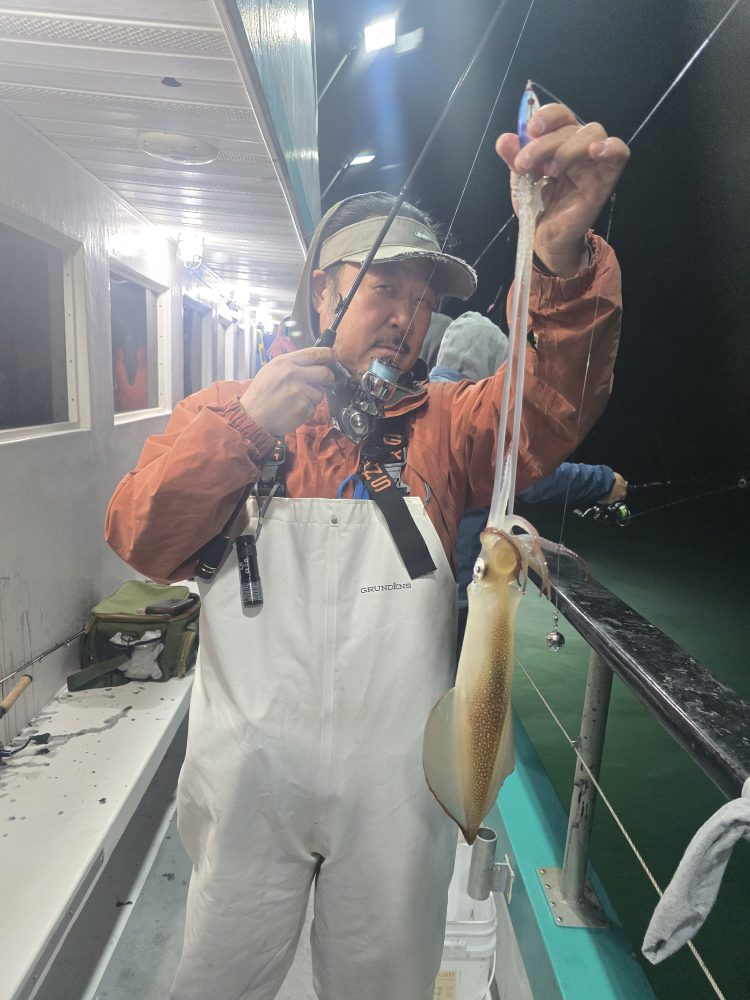 Person in fishing gear holds a squid on a boat at night.