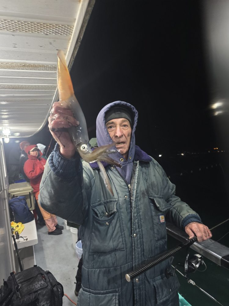 Person in a hooded jacket holding a squid on a boat at night.