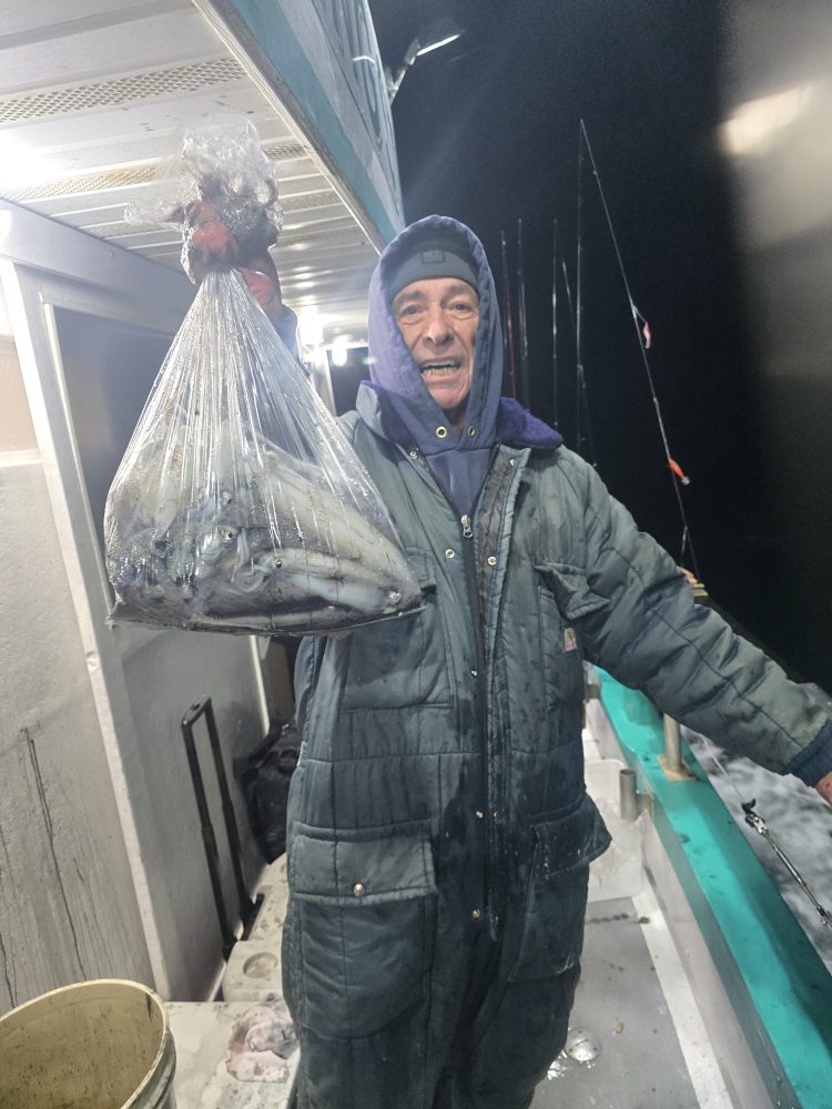 Person in a coat holding a bag of fish on a boat at night.