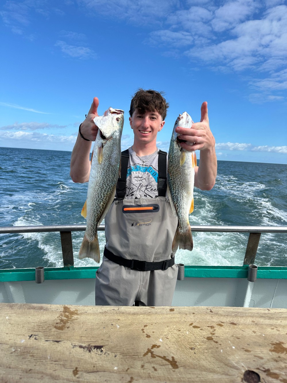 Person on a boat holding two fish with the ocean in the background.
