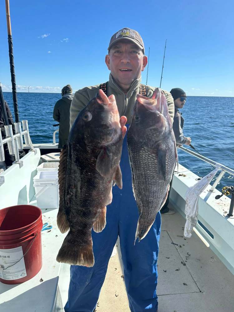Man on boat holding two large fish with ocean in the background.