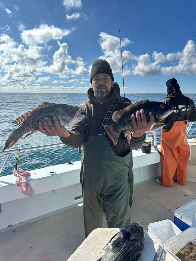 Man on boat holding two fish with ocean and cloudy sky background.