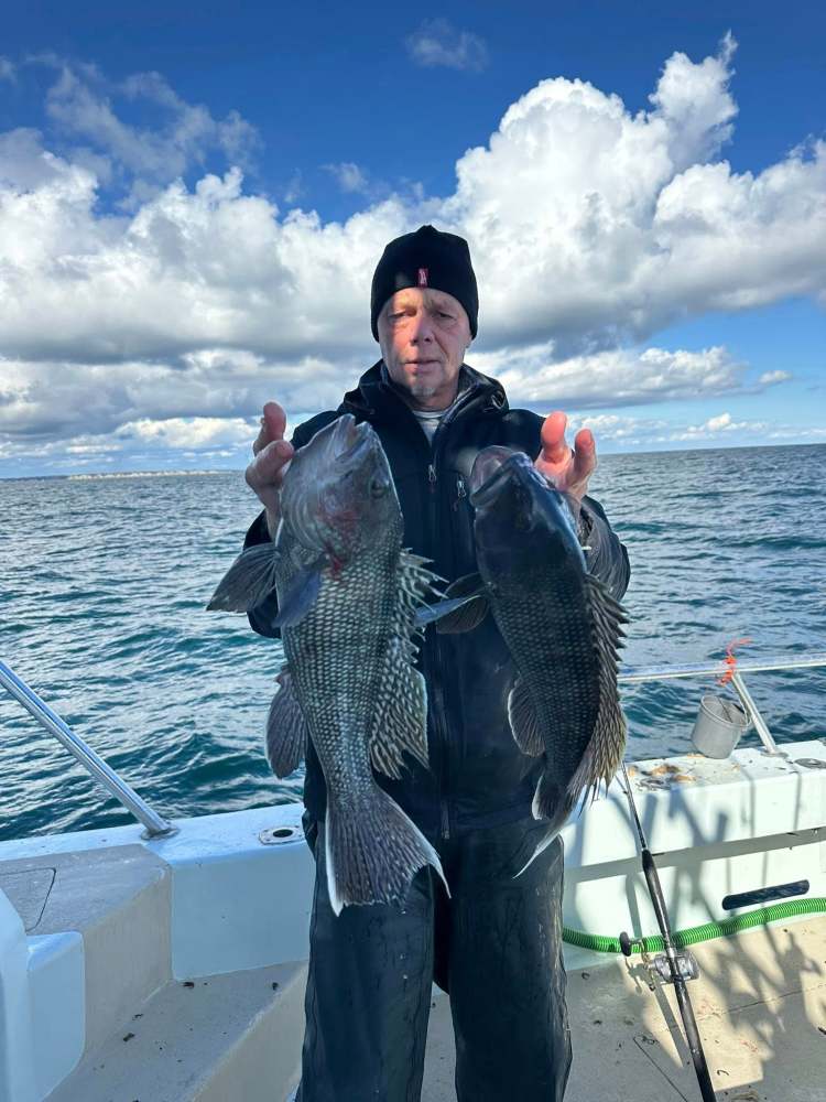 Person holding two large fish on a boat under a cloudy sky.