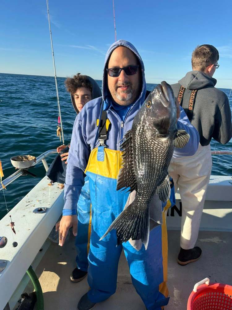 Man in blue and yellow gear holding large fish on a boat with two others fishing nearby.