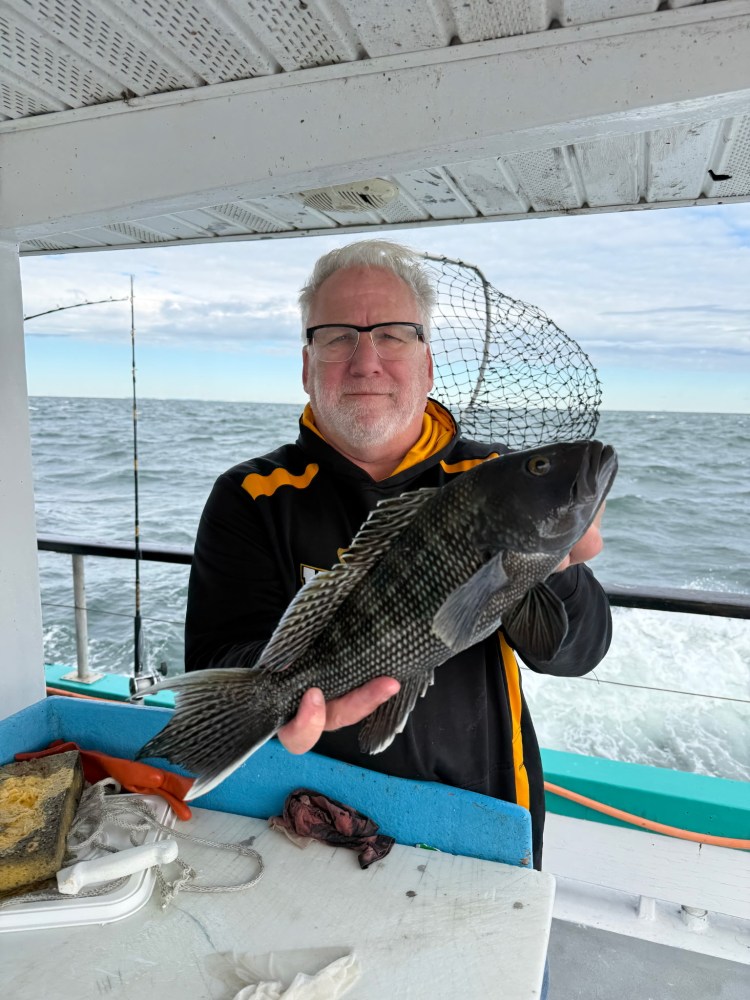 Person holding a large fish on a boat with ocean in the background.
