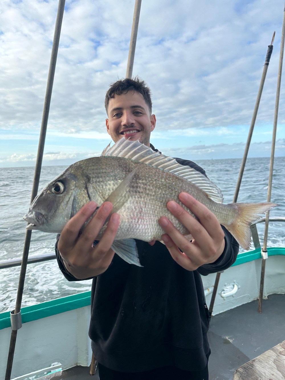 Person holding a fish on a boat with cloudy sky and ocean in the background.