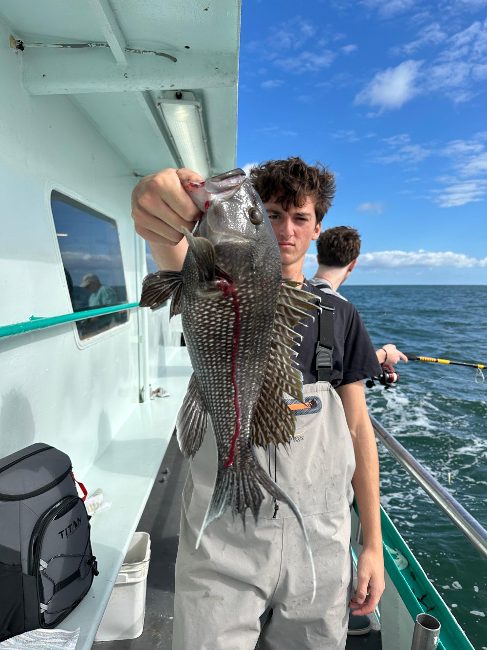 Person holding a fish on a boat with ocean in background under a blue sky.