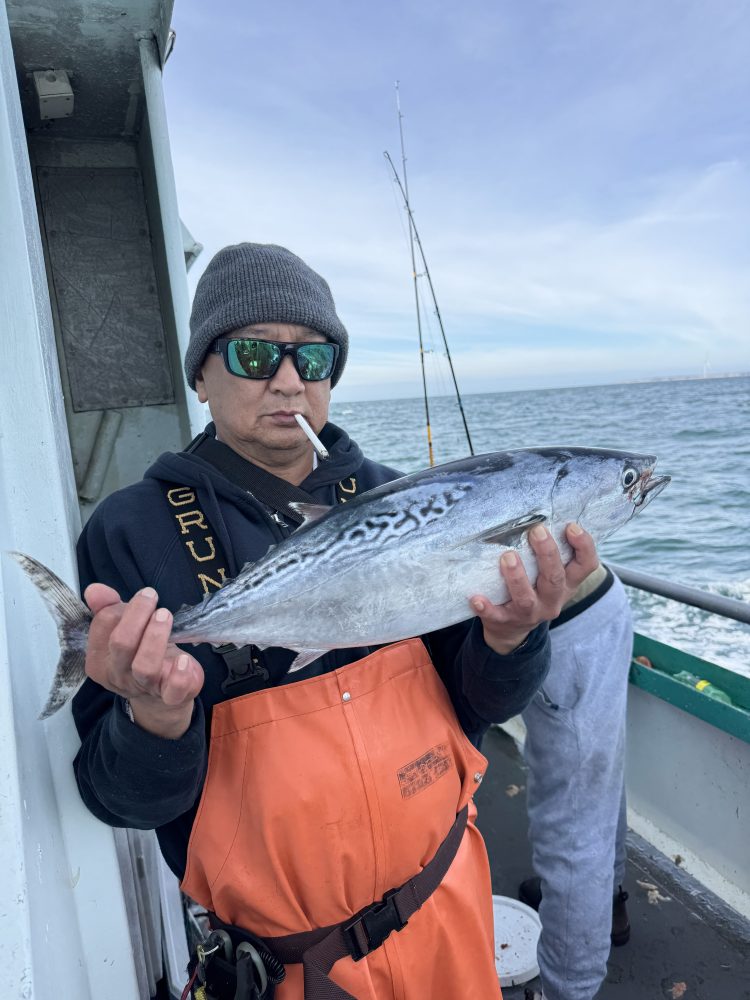 Person in orange overalls on a boat holding a fish with ocean in the background.