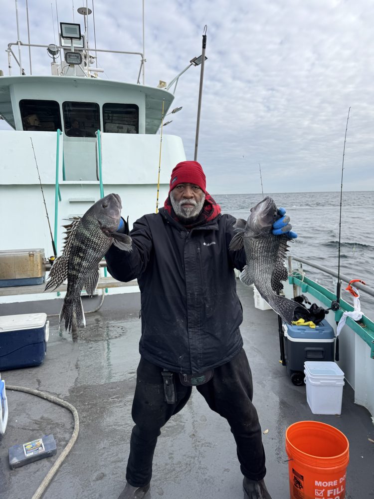 Person in a red hat holding two fish on a boat deck, with sea and cloudy sky in the background.