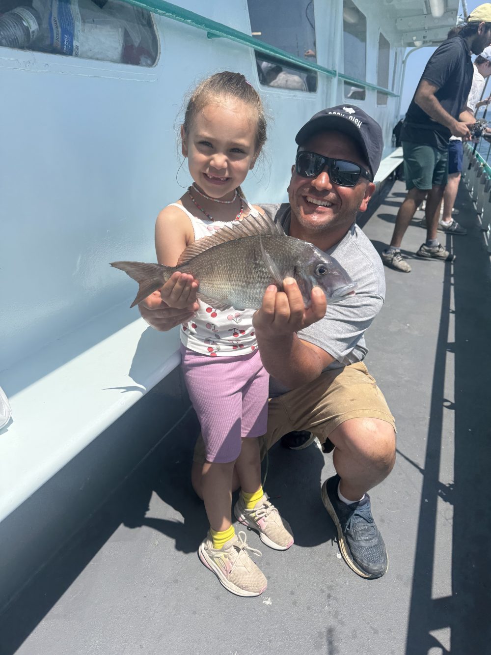 Smiling man and child holding a fish on a boat deck.